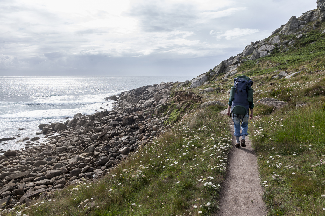 A backpacker on her way in Cornwall hills on the coast by the Celtic Sea